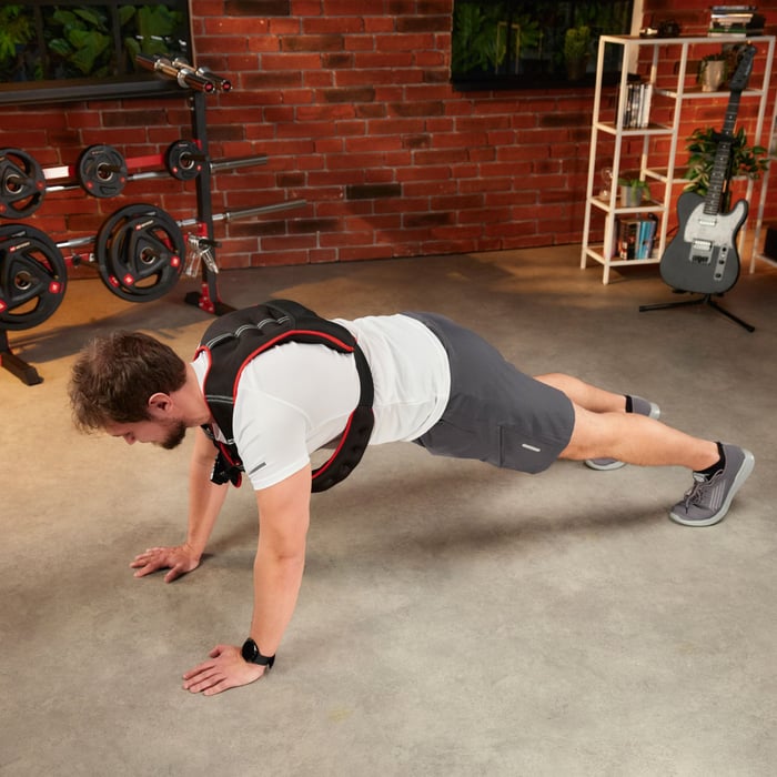 A man performing a plank or push-up exercise wearing a weighted vest to increase workout intensity in a home gym.