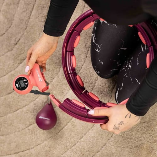 Zbliżenie na ręce kobiety montującej hula hop z wypustkami i licznikiem – nowoczesny model do ćwiczeń w domu. Hula hop z wypustkami – efekty ćwiczeń zależą od regularności treningów.