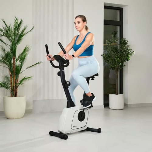 Kobieta ćwicząca na białym rowerze treningowym w jasnym, nowoczesnym wnętrzu – przykład klasycznego modelu do lekkiego cardio, idealny do porównania: rower treningowy czy spinningowy