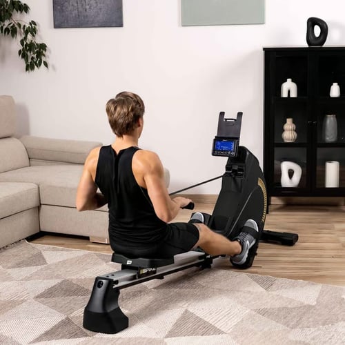 Mężczyzna w czarnym stroju trenuje na nowoczesnym wioślarzu w przestronnym salonie – przykład, jaki wioślarz do domu sprawdzi się do intensywnych treningów siłowych i cardio.