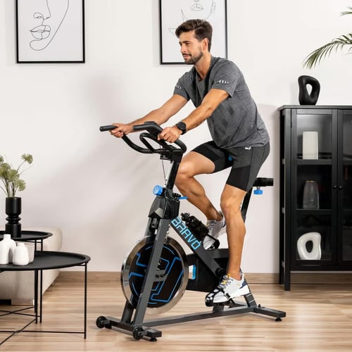 Mężczyzna podczas spinning treningu w domowym wnętrzu, ćwiczący na czarno-niebieskim rowerze stacjonarnym Bravo – idealna forma aktywności cardio i spalania kalorii.