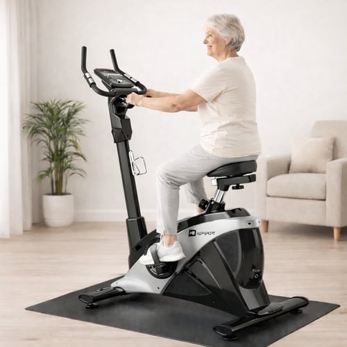 Starsza kobieta ćwiczy w domu na pionowym rowerze stacjonarnym z ergonomicznym siodełkiem — idealna propozycja dla osób szukających, jaki rower stacjonarny dla seniora wybrać.