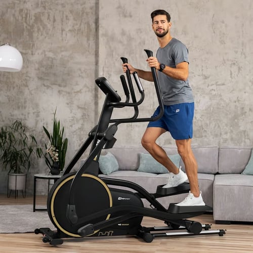 Mężczyzna ćwiczący w domu na czarnym trenażerze eliptycznym z żółtym detalem — trenażer eliptyczny co to, przykład nowoczesnego sprzętu do treningu cardio.