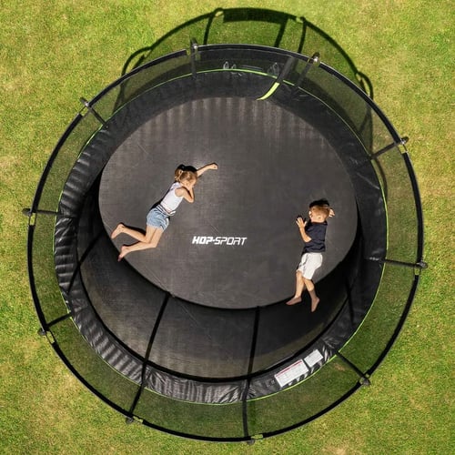 Widok z góry na dwoje dzieci leżących na środku trampoliny ogrodowej Hop-Sport z siatką ochronną – trampolina ogrodowa czy warto dla relaksu i ruchu w ogrodzie.