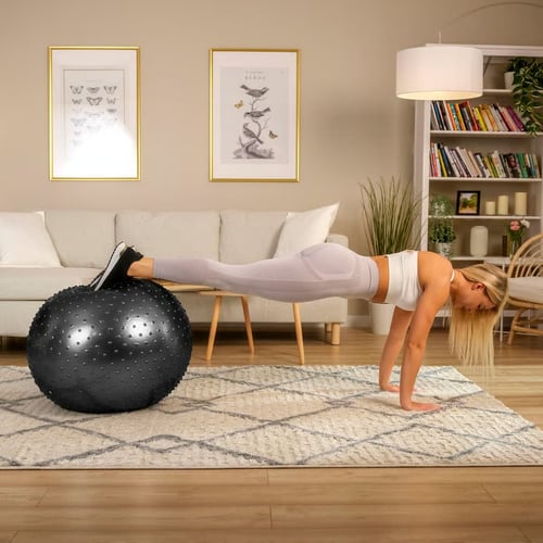 Kobieta w pozycji deski z nogami na czarnej piłce gimnastycznej z wypustkami – ilustracja, jak piłka gimnastyczna jaki rozmiar wpływa na stabilność i trudność ćwiczeń.