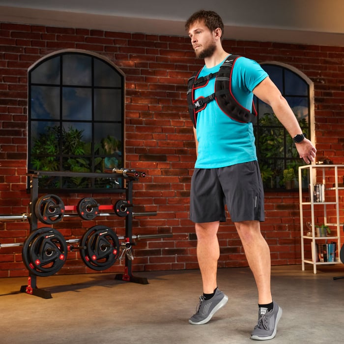 Full body view of an athlete doing weighted jumps or calf exercises with a black and red weighted vest for extra resistance.