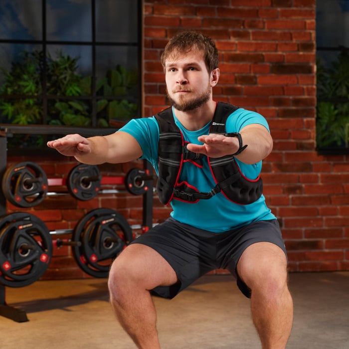 A man performing a squat exercise in a gym while wearing a black weighted vest.