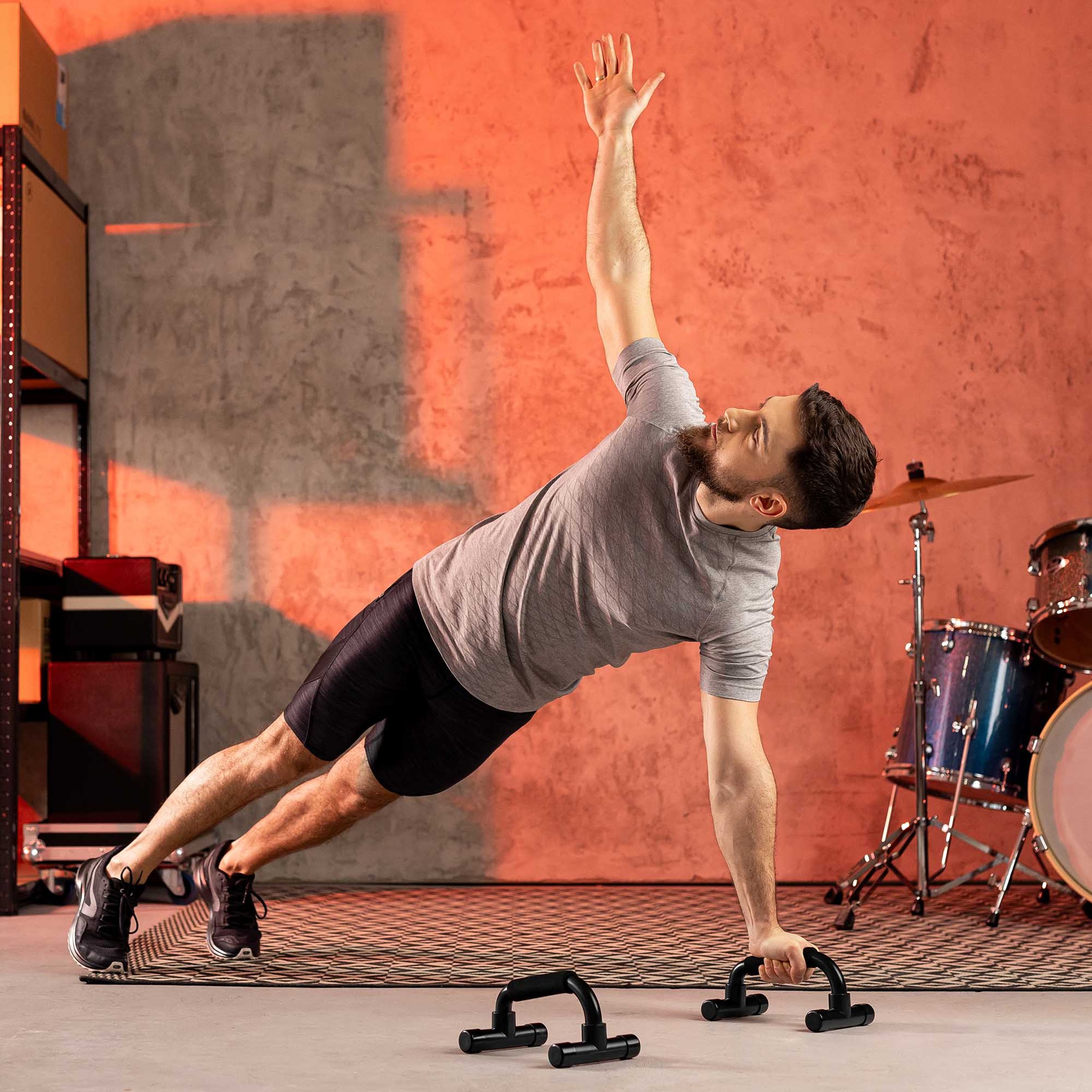 Ein Mann führt eine Side-Plank aus, während er einen schwarzen Hop-Sport Liegestützgriff hält. Im Hintergrund befinden sich eine Trommel und Regale.