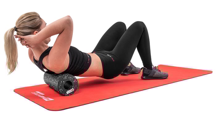 Kobieta roluje mięśnie pleców za pomocą wałka o długości 33cm czarnego w białe kropki